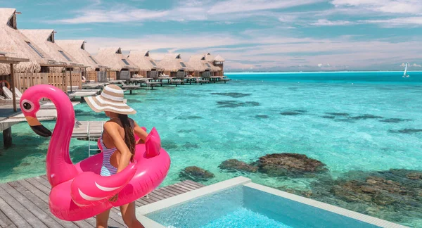 Travel vacation fun tourist woman enjoying luxury summer holidays at Bora Bora overwater bungalow swimming with flamingo pool toy float at infinity pool by turquoise ocean. Tahiti getaway destination. — Stok fotoğraf