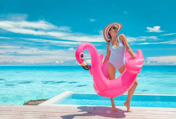 Summer pool fun swimsuit model posing in pink flamingo float showing off slim figure bikini ready body for luxury Caribbean vacation getaway. Woman having fun by hotel infinity pool. — 스톡 사진