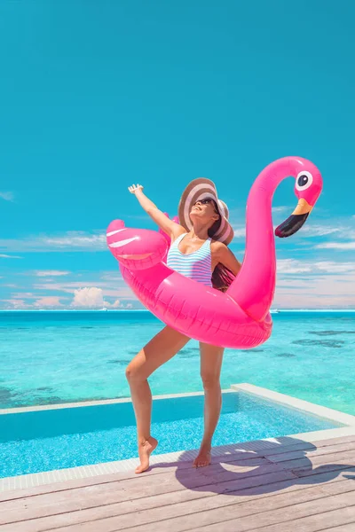 Summer happy woman relaxing sunbathing at luxury infinity pool swimming with pink funny flamingo float. Joyful tanning girl in swimsuit on hotel Caribbean vacation. — Photo