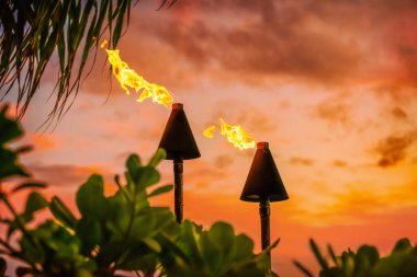 Hawaii luau party Maui fire tiki torches with open flames burning at sunset sky clouds at night. Hawaiian cultural travel vacation background. clipart