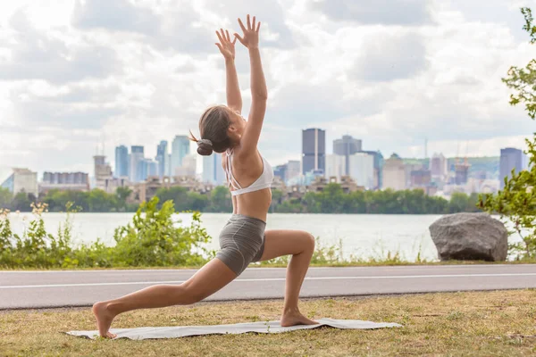 Corso di yoga benessere all'aperto in città parco donna facendo alta lunge mezzaluna posa sul tappeto esercizio all'aperto contro skyline vista sul fiume — Foto Stock