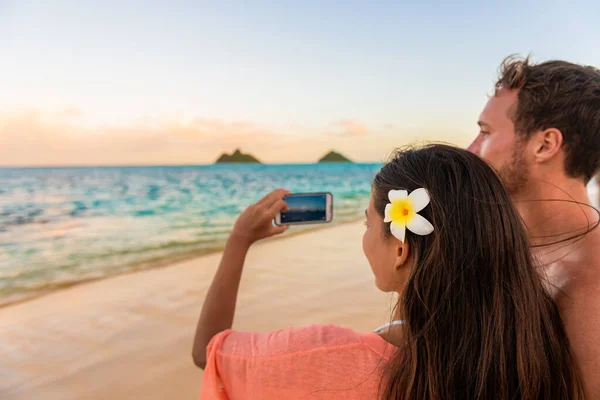 Χαβάη τουρίστες διακοπές λήψη φωτογραφιών με το τηλέφωνο για ρομαντική βόλτα στο ηλιοβασίλεμα στην παραλία Lanikai, Oahu, Χαβάη ταξίδι του μέλιτος απόδραση. Ζευγάρι τρόπο ζωής. — Φωτογραφία Αρχείου