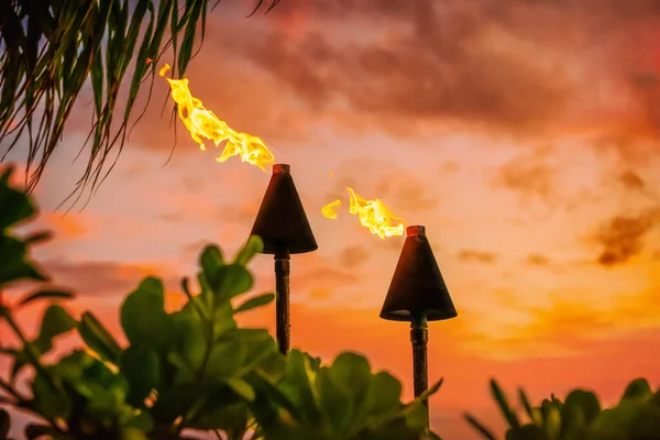 ハワイのルアウパーティーマウイの火のティキのトーチは、日没の空の雲で夜に燃えています。ハワイ文化旅行休暇の背景. — ストック写真