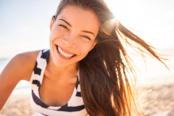 Mujer asiática feliz sonriendo en sol llamarada playa modelo de belleza natural con dientes perfectos riendo de alegría y diversión en las vacaciones de verano. Cabello largo castaño sano en el resplandor de la puesta del sol. — Foto de Stock