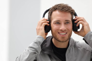 Man putting on headphones to listen to music mobile phone app. Happy smiling young urban person wearing headset sing smartphone mobile app listening to songs in living room at home clipart