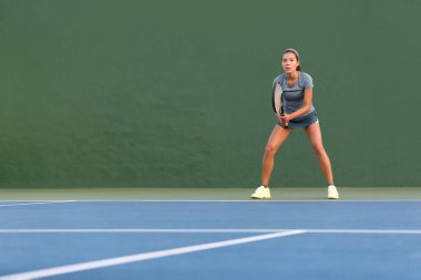Tennis player woman standing ready to play waiting to receive serve. Outdoor fitness instructor focused playing on hard court on green background clipart