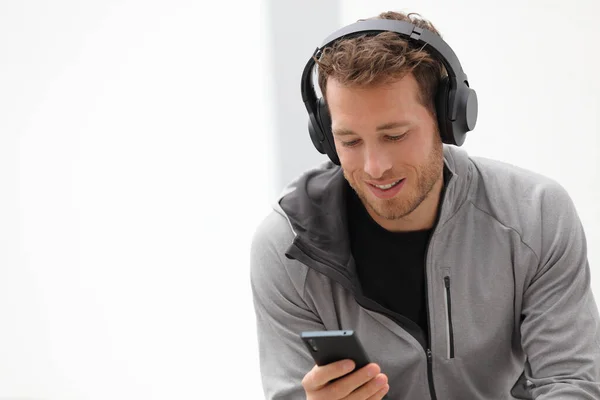 Man lyssnar på musik mobiltelefon app bär headset sitter hemma. Friska livsstil idrottsman med hjälp av smartphone på jogging paus utomhus koppla av i avslappnade kläder — Stockfoto