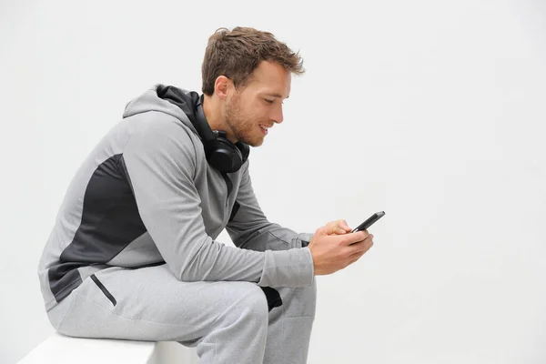 Fitness man using phone app on jogging break relaxing at home outdoors. Active lifestyle young adult holding smartphone watching online video or texting sms messages — Stock Photo, Image