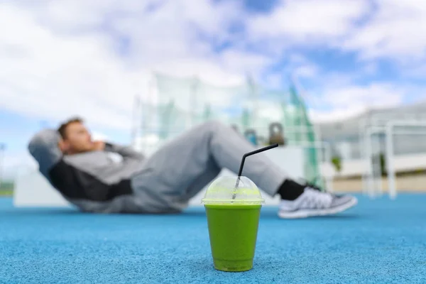 Fitness hombre entrenamiento en el gimnasio con licuado verde bebida de desintoxicación haciendo ejercicios de abdominales en el suelo al aire libre — Foto de Stock