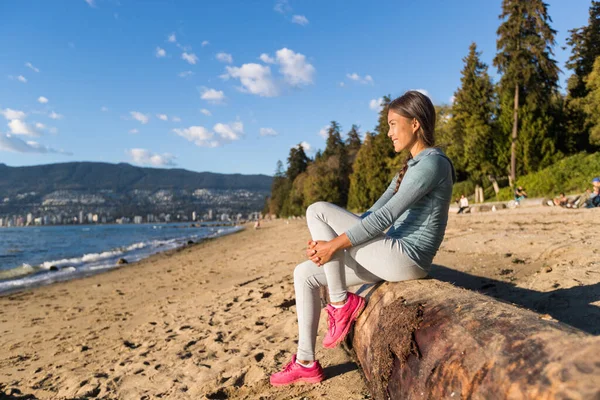Vancouver urban lifestyle woman relaxing on Third Beach in Stanley Park, Vancouver, BC, Canada. Canadian Asian girl sitting on tree trunk at popular sandy resting area of canadian city — Stock Photo, Image