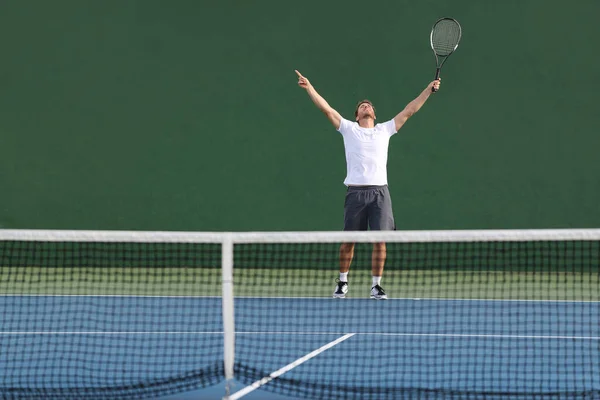 테니스 선수가 초록색 실외 코트에서 팔을 들고 기뻐하며 우승하는 모습 — 스톡 사진