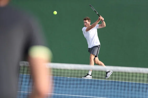 Tenista muž bít backhand vracející míč s raketou na zeleném pozadí. Sportovní muži hrají spolu na venkovním hřišti — Stock fotografie