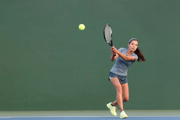 Tenis jugando a la mujer golpeando pelota en la cancha dura verde. Asiática atleta chica volver servir con raqueta usando skort y zapatos — Foto de Stock