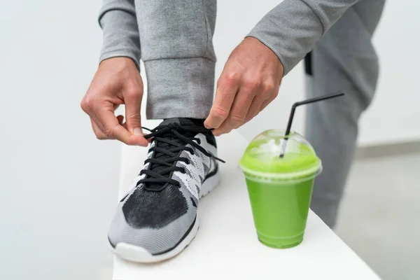 Koşu ayakkabıları ve yeşil smoothie kahvaltı bağlayan fitness adamı. Sağlık kilo verme sporcusu yeşil meyve suyu içiyor spor ayakkabıları bağcıklarını etkin yaşam tarzına hazır hale getiriyor. Sabah aktif yaşam tarzı — Stok fotoğraf
