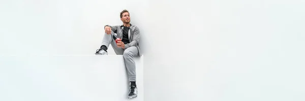 Ftiness sport człowiek picia smoothie trening baner relaks w domu w siłowni jogging spodnie aktywne ubranie na świeżym powietrzu. Sportowiec siedzący na białym tle — Zdjęcie stockowe