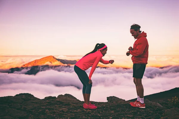 Lopers moe uitgeput tijdens cardio-inspanning met behulp van hun draagbare technologie smartwatch controleren hartslag monitor. Twee atleten paar samen hardlopen in de buitenlucht bergen landschap — Stockfoto