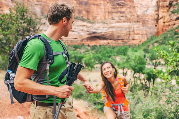 男人在旅行时帮助女朋友爬上岩石.徒步旅行者- -年轻人牵着手寻求帮助。挑战和团队支持概念 — 图库照片