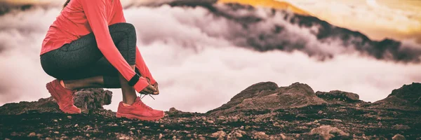 Runner smartwatch mujer preparándose para el sendero correr en las altas nubes frías montañas fondo atando cordones zapatillas de running. Fitness y motivación deportiva estilo de vida saludable. Banner cultivo panorámico —  Fotos de Stock