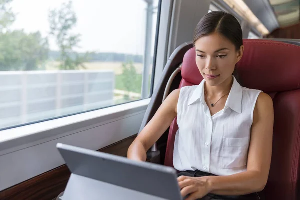 Empresaria trabajando en la computadora portátil en tren. Escritor o diseñador independiente asiático que escribe correos electrónicos en la computadora mientras viaja a la reunión en la ciudad. Viajes urbanos de mujer viajera —  Fotos de Stock