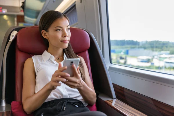 Asiatin entspannt sich im Zugsitz, während sie Smartphone-App benutzt Chinesische Geschäftsfrau genießt das Ansehen von SMS auf dem Handy. Lebensstil auf Reisen — Stockfoto