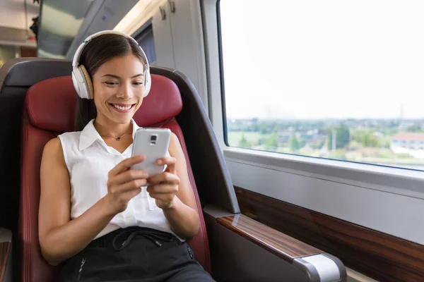 Moderna människor stadslivsstil. Ung urban kvinna som använder telefon app och trådlösa hörlurar för att lyssna på musik eller spela tv-spel online. Asiatisk flicka njuter av tågresor i business class sits — Stockfoto