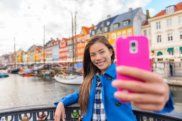 Selfie chica turística tomando fotos con el teléfono en Copenhague Nyhavn, famosa atracción turística de Europa. Mujer asiática visitando el antiguo canal de agua frente al mar en Kobenhavn, Dinamarca, Escandinavia. —  Fotos de Stock