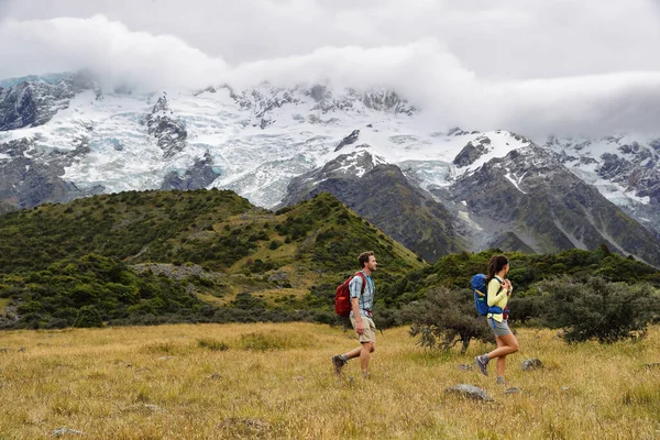 Nowozelandzcy turyści wędrujący po zaśnieżonym górskim tle krajobrazu. Para tramperów spacerujących po Hooker Valley Track, popularnym miejscem turystycznym na letnie wakacje — Zdjęcie stockowe