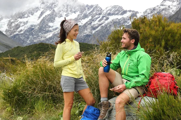 Camping lifestyle young people eating lunch outdoors hiking on New Zealand mountain trail track. Couple trampers tramping in nature with backpacks — Stock fotografie