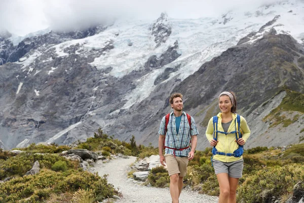 New Zealand backpackers tramping on Mount Cook Aoraki Hooker valley travel. Backpacking hikers hiking walking on Hooker Valley Track. Snow capped mountains glacier landscape. Couple on summer hike — Stock fotografie