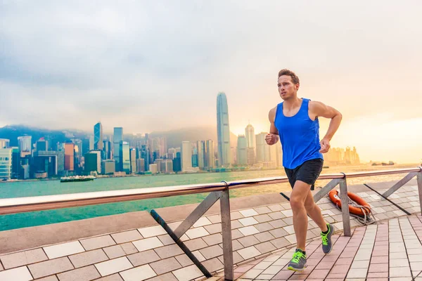 在香港城市的天际线上跑步的男子运动员.香港维多利亚港长廊上训练健美操的白人运动员将于夏至下午在日落时分在长廊上慢跑 — 图库照片
