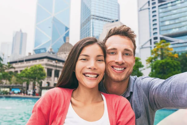 Selfie foto de viaje con teléfono de adultos jóvenes turistas enamorados sonriendo a la cámara. Pareja interracial en la ciudad de Hong Kong, vida urbana. Asiático multirracial chino mujer, caucásico hombre en su 20s —  Fotos de Stock