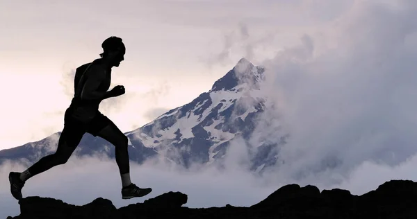 Running man athlete trail running in mountain summit background. Male runner on run training outdoors living active fit lifestyle. Silhouette at sunset — Stockfoto