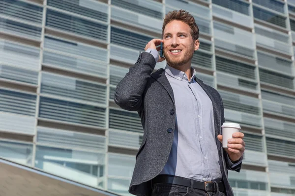 商人专业行政人员通过电话谈生意.在城市背景下，穿着西装的男人在用智能手机打电话，微笑着在城市的办公大楼里喝咖啡 — 图库照片