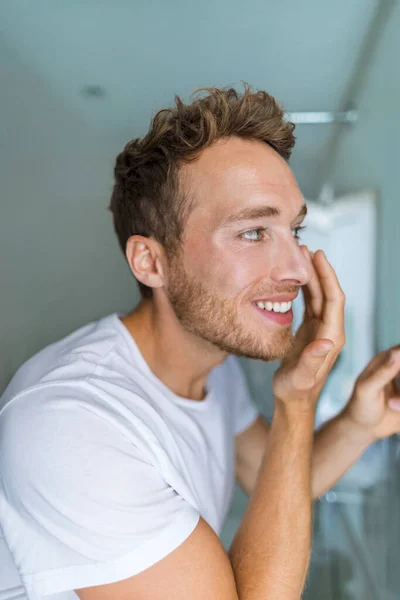 Hombre poniendo bajo crema para los ojos en la cara cuidando su piel, Tratamiento anti-envejecimiento en casa. Mañana rutina joven belleza masculina estilo de vida — Foto de Stock