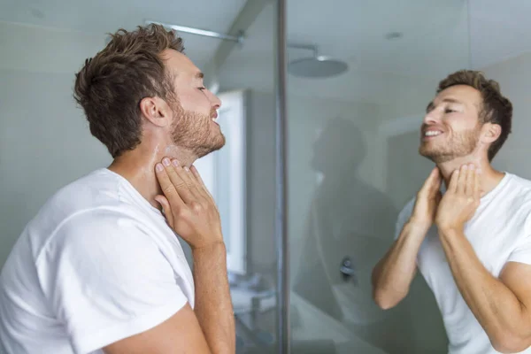 Uomo mettere dopo barba lozione profumo o crema per la cura della pelle per la pelle sensibile dopo la barba da barba guardando nello specchio del bagno sul collo. Bellezza maschile, cura della barba concetto di cura della pelle — Foto Stock