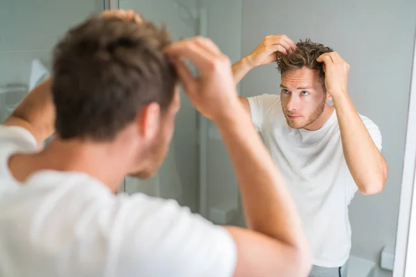 バスルームミラーを見て脱毛の男は、ワックスが彼の髪のスタイリングに触れるか、脱毛の問題をチェック置く。脱毛の男性問題 — ストック写真