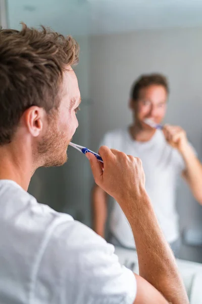 Ο άνθρωπος βουρτσίζει τα δόντια του το πρωί κοιτάζοντας στον καθρέφτη του μπάνιου χρησιμοποιώντας οδοντόβουρτσα και οδοντόκρεμα. Οικιακός τρόπος ζωής, οδοντιατρική φροντίδα. Προφορική υγεία — Φωτογραφία Αρχείου