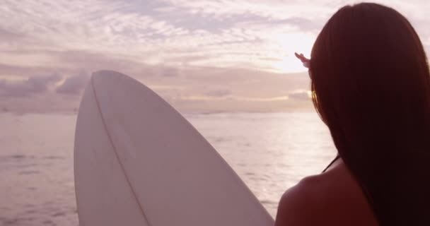 Девушка-серфер занимается серфингом, глядя на восход солнца на океанском пляже — стоковое видео