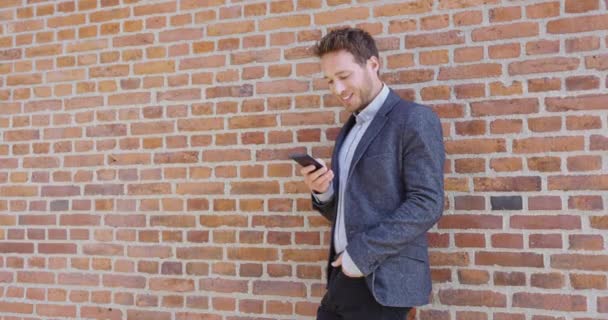 都会でスマートフォンを使う若いビジネスマン｜バックグラウンドレンガの壁 — ストック動画