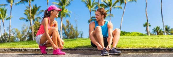 Runners couple tying running shoes to run banner. Runner woman and athlete man lacing shoe laces at park. Healthy lifestyle jogging motivation, happy healthy people. Horizontal landscape crop — Stockfoto