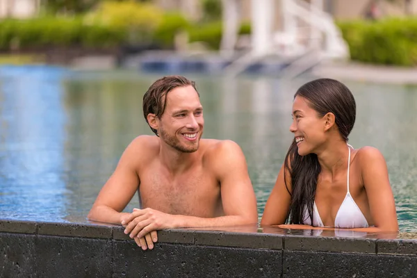 Pool couple relaxing on luxury resort travel holiday talking together on summer vacation. Asian woman, caucasian man in love — Stock Photo, Image