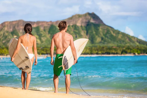 Los surfistas de Hawaii se relajan en la playa de waikiki con tablas de surf mirando las olas en Honolulu, Hawaii. Estilo de vida saludable activa pareja fitness al atardecer con diamante cabeza montaña en el fondo —  Fotos de Stock