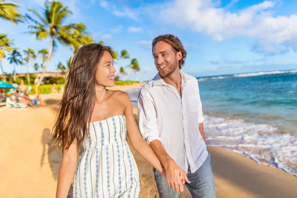 Beach couple happy holding hands on hawaiian holidays in Waiohai beach, Poipu in Kauai, Hawaii, USA. Newlyweds people in love on honeymoon. Asian woman, Caucasian man — Stockfoto