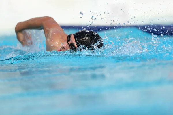 Entrenamiento de atleta de piscina en interiores para competición profesional. Hombre nadador en la práctica de natación en el estadio haciendo gatear con el brazo salpicando agua. Copiar espacio sobre fondo de agua azul —  Fotos de Stock