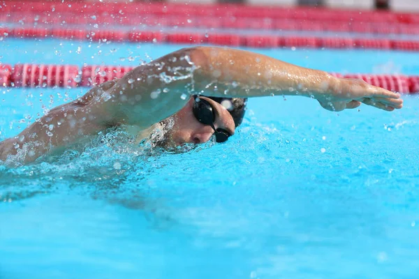 游泳池运动员在做爬泳.男子游泳运动员，带着护目镜和帽子在体育场进行训练，以便进行锻炼。有氧运动 — 图库照片