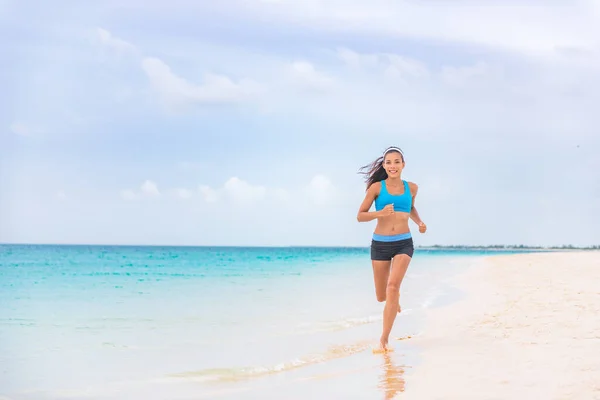 Exercise fitness athlete woman jogging on beach training cardio in summer vacation background. Blue ocean water, sun sky landscape. Happy Asian girl running barefoot outside — Stock fotografie