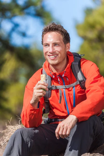 Hiker man healthy outdoor lifestyle eating muesli bar during hike on mountain hiking. Happy people eat granola cereal bar snack living active lifestyle in nature — Stockfoto