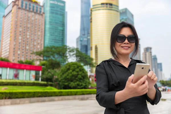 Mobile phone city lifestyle busy real estate chinese businesswoman lady texting using 5g app. Asian business woman walking in Shanghai street, China. Happy smiling person in her 50s work commute — Photo