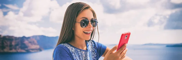 Happy young woman relaxing in summer sun texting using mobile phone outdoor at Santorini luxury hotel view of Mediterranean Sea. Banner panorama landscape — Stockfoto