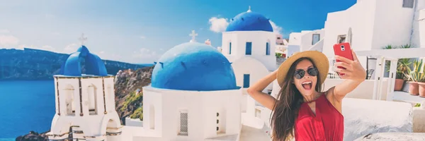 Счастливый турист делает селфи, веселясь на европейском летнем отдыхе на Санторини, круизном направлении с панорамным баннером. Азиатка забавно держит мобильник, фотографируя — стоковое фото